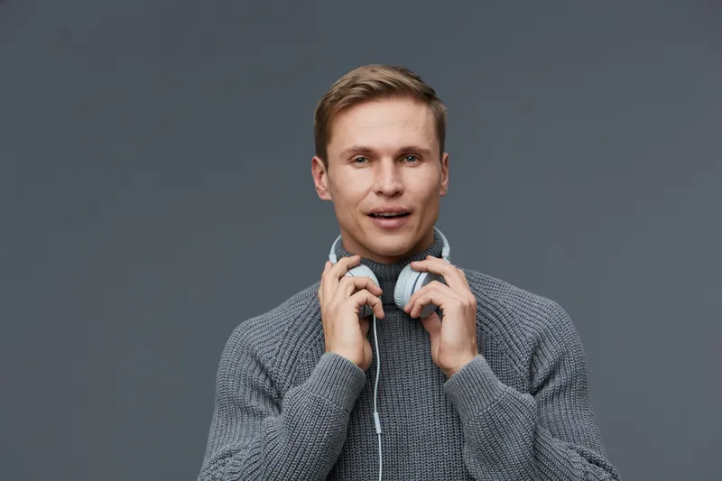 young man wearing gray sweater hold headphones look camera with slight smile isolated on dark gray background concept of digital detox and mental health with gadgets