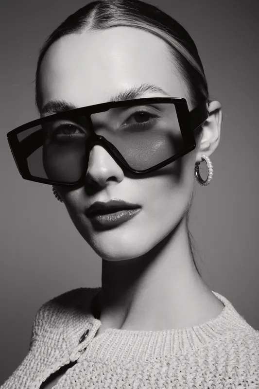 Close-up portrait of a young white woman wearing oversized sunglasses and hoop earrings in black and white. Fashion concept with stylish accessories and confident look.