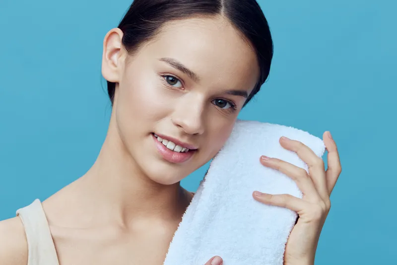 Young woman with a towel smiling against a blue background, embodying skincare and beauty concepts for healthy lifestyle imagery
