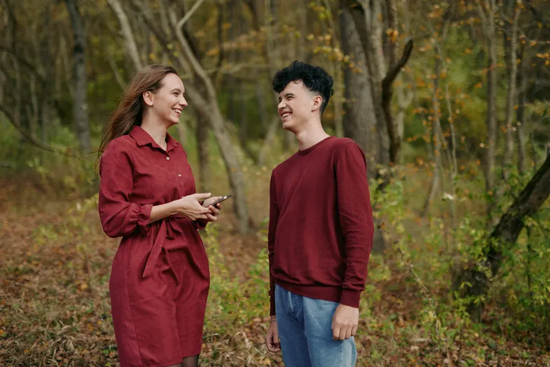 A candid outdoor portrait of two young people smiling and sharing a warm moment in an autumn forest, conveying natural, believable interaction, genuine expressions and ?????????????