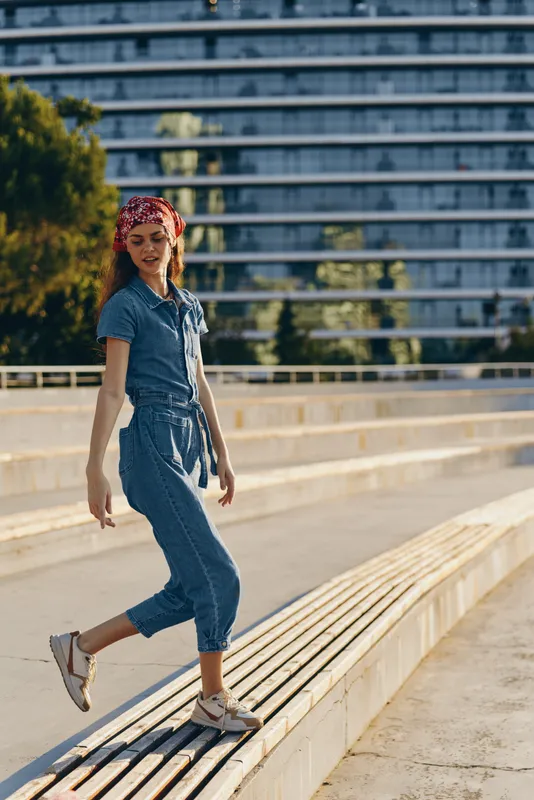 Lifestyle woman in modern boho-western denim street style walking outdoors with relaxed smile and film color tones, casual urban vibe, youthful and carefree.