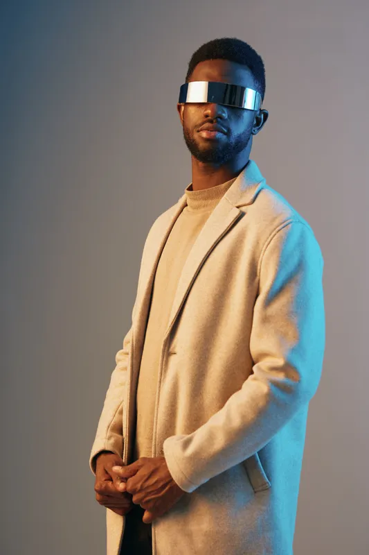 Stylish young man wearing futuristic glasses and a chic coat, showcasing modern fashion trends with a colorful background, perfect for fashion or technology themes