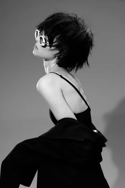 Stylish woman in sunglasses posing in black and white with elegant outfit and short hair.