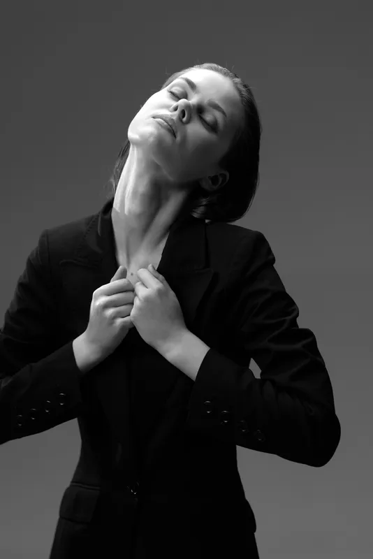 Black and white portrait of a woman in a dark jacket showing emotion and elegance against a plain background.