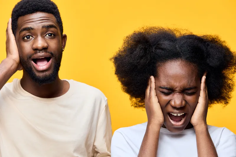 Two diverse people expressing frustration with loud noise, wearing casual clothing against a bright yellow background, capturing emotion and modern style