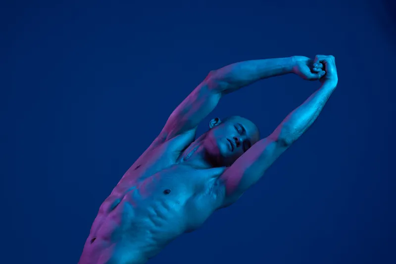 A striking image of a male dancer in an energetic pose against a blue backdrop, showcasing strength and movement with a captivating light display.