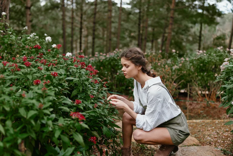 Young woman enjoying nature in a lush garden, wearing stylish shorts and a white shirt, surrounded by vibrant flowers, evoking a sense of tranquility and connection with nature