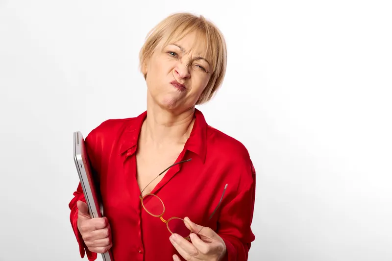 Woman holding toothbrush in red robe, grimacing with hand near cheek, isolated on white background, dental hygiene concept, oral care routine, discomfort and pain