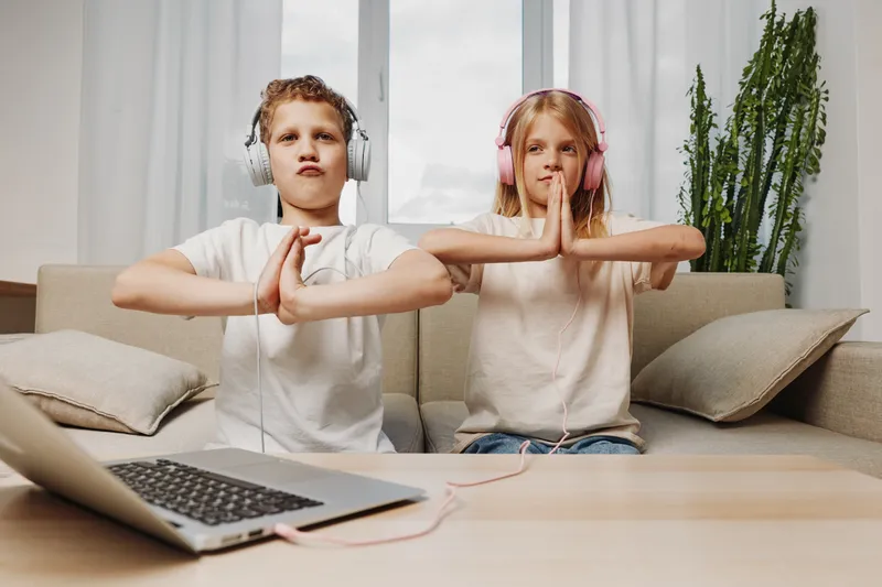 Two kids with headphones practicing meditation and mindfulness at home sitting on sofa in casual clothes. Concept of relaxation, focus, and digital wellness for children.