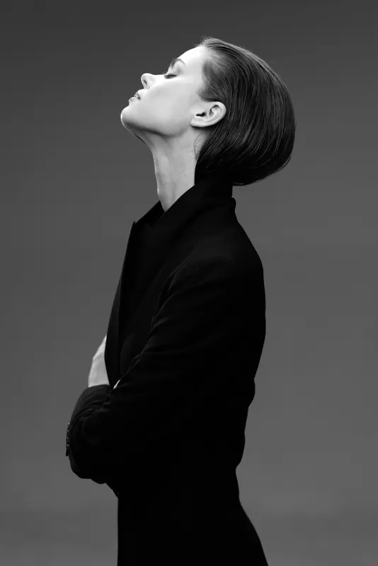 Black and white elegant woman with short hair posing in profile against dark background in stylish outfit.