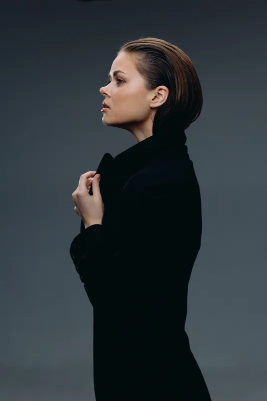 Profile of a woman wearing a black turtleneck, posing confidently against a dark gray background.