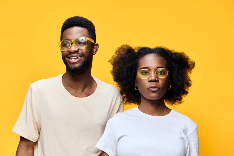 Happy African American couple wearing trendy glasses against vibrant yellow background, showcasing fashion and cheerful emotions, perfect for contemporary lifestyle themes
