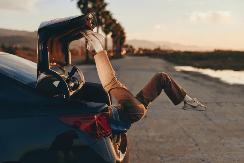 Woman lifestyle beside car driving at sunset on an open road outdoors casual comfort freedom for travel commuting golden light evening roadside view