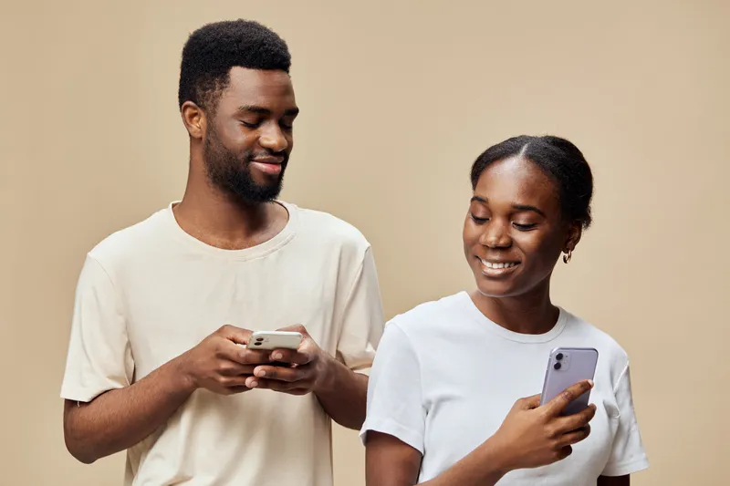 Two young adults engaged in a joyful smartphone conversation, showcasing happiness and connection against a warm beige background