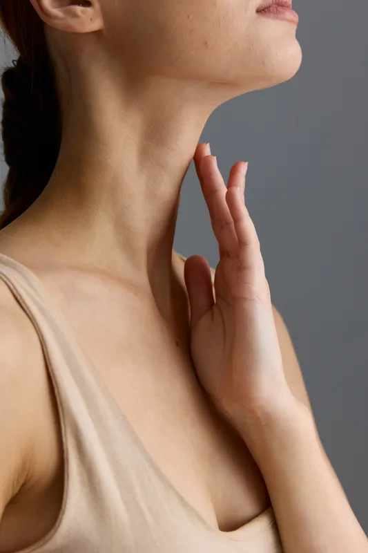woman neck close-up with hand touching smooth skin and natural texture on gray background, showing beauty and care in soft neutral tones, skin health focus