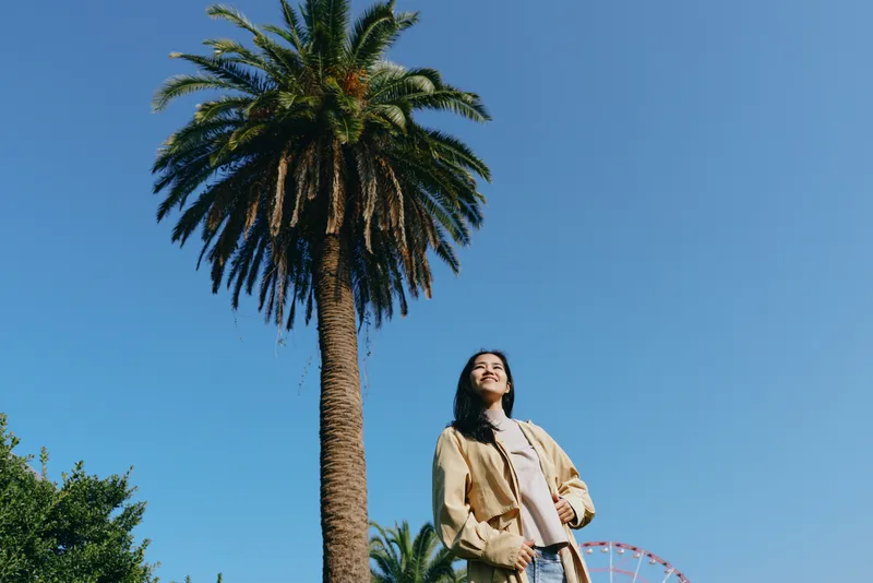 Palm tree backdrop, outdoor setting under clear sky, woman in casual fashion poses in sunlight, relaxed park vibe, nature lifestyle scene ideal for travel, leisure, and outdoor photography