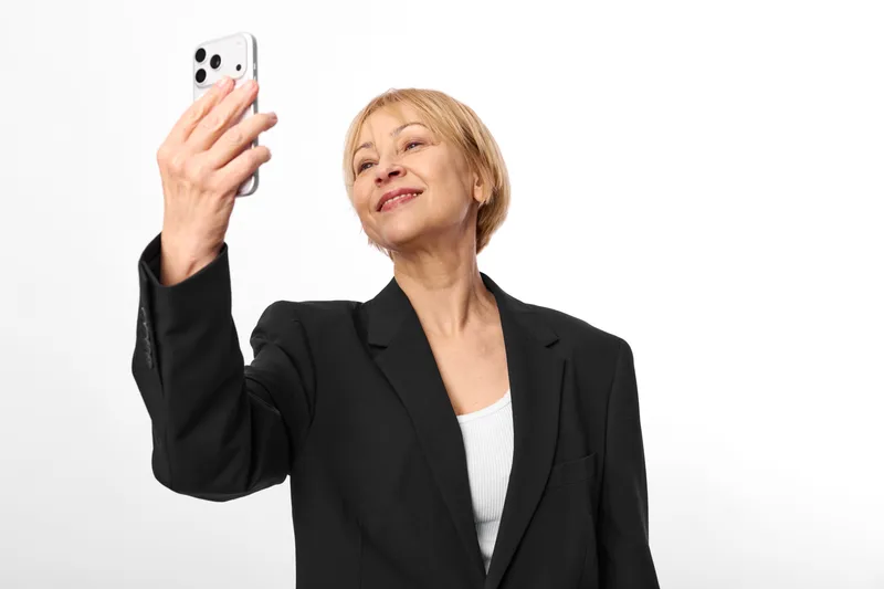Senior woman portrait holding smartphone, black blazer business style, looking at screen, communication and technology concept, isolated on white background