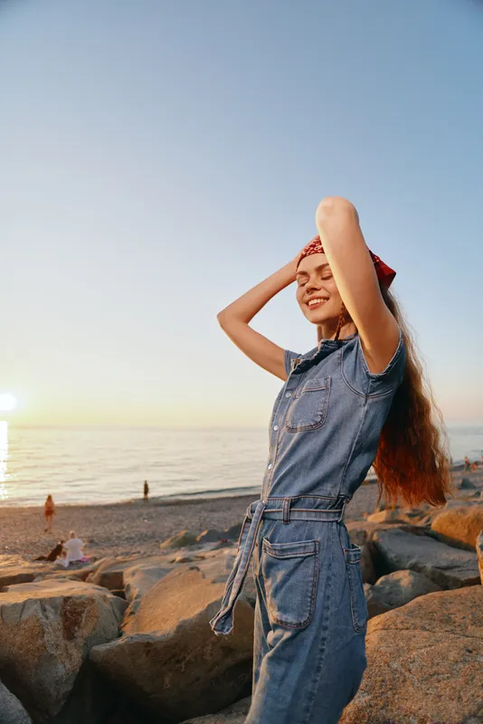 Lifestyle woman in modern boho-western denim street style enjoying a sunny beach with relaxed pose and film color warm tones at sunset.