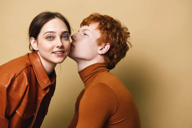 Couple, young man and woman close together with affectionate gesture and smile, casual clothing and warm tones for love and relationship in studio interior.