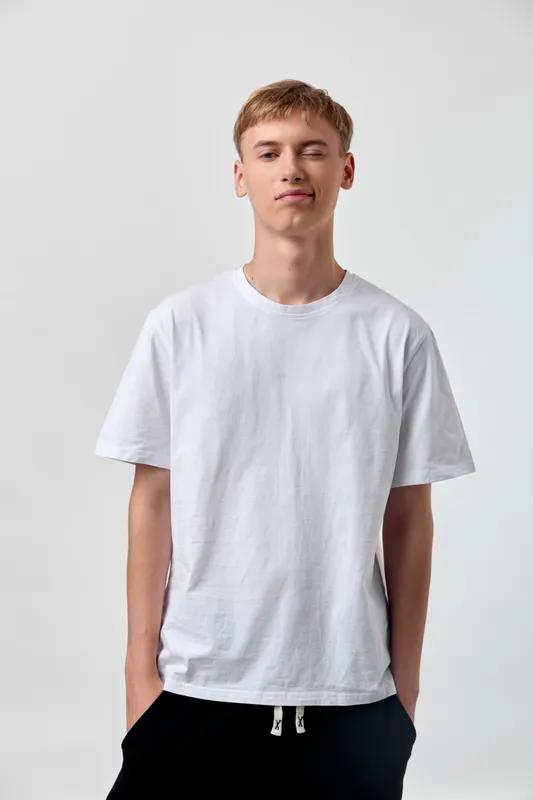 White t shirt male model in casual clothing stands against a blank background, showcasing a clean and relaxed look for everyday wear, minimal style, and studio photography suitable for fashion and