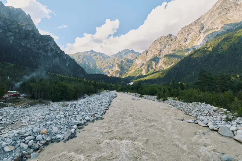 A scenic river winds through a rocky valley framed by towering mountains under a bright sky, creating a serene and majestic natural landscape that invites exploration and wonder.