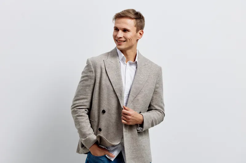 Smiling man wearing a light-colored blazer and white shirt looking away against a plain white background, studio portrait, casual fashion style, cheerful mood, male model.