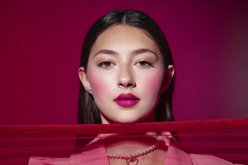 Close-up of a young woman with bold bright makeup and dark hair against a red background. Creative fashion and beauty concept focusing on fierce lips and flawless skin.