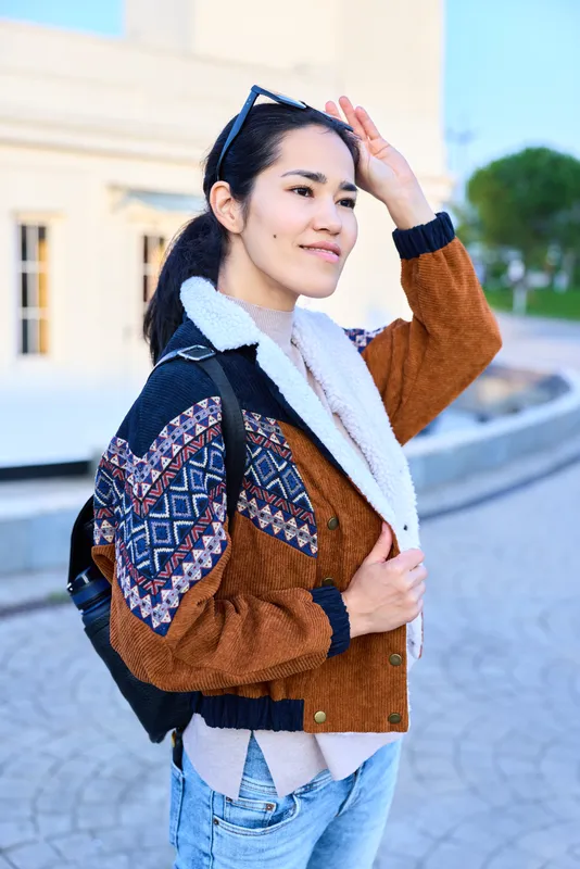 Woman wearing a patterned jacket and sweater, outdoors with backpack, street style and casual fashion for everyday urban adventures in daylight near architecture