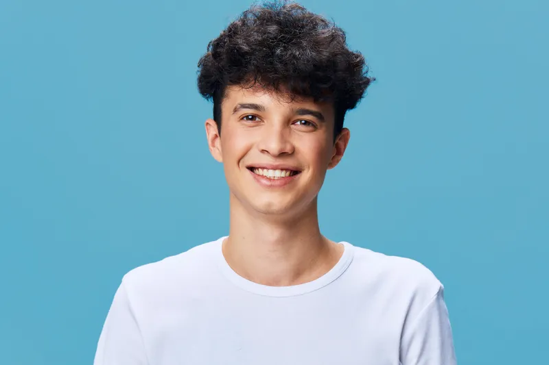 smiling man with curly hair wearing white t-shirt on blue background, casual young adult, cheerful expression, studio portrait, isolated