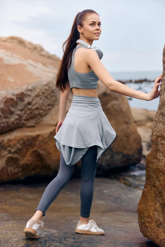 Athletic woman in gray workout clothing posing on rocky beach, showcasing confidence and fitness, perfect for healthy lifestyle and activewear concepts