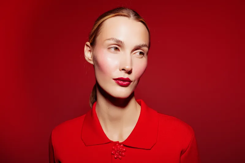 Portrait of a woman with red lipstick and red sweater on red background. Studio lighting highlights her clear skin and elegant expression. Fashion and beauty concept.