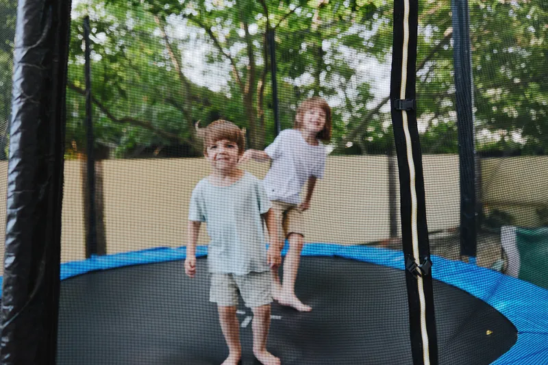 Happy children playing on a trampoline, enjoying a sunny day outdoors with greenery in the background and vibrant colors around them.
