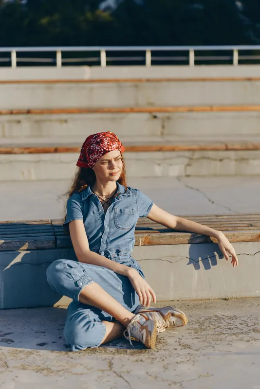 Lifestyle woman in modern boho-western denim street style sitting outdoors with relaxed posture, casual vibe, and warm film color tones