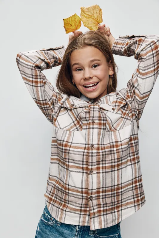 Girl with smiling face holding yellow autumn leaves above head wearing plaid shirt and jeans in studio with white background for seasonal fall concept and childhood fun.