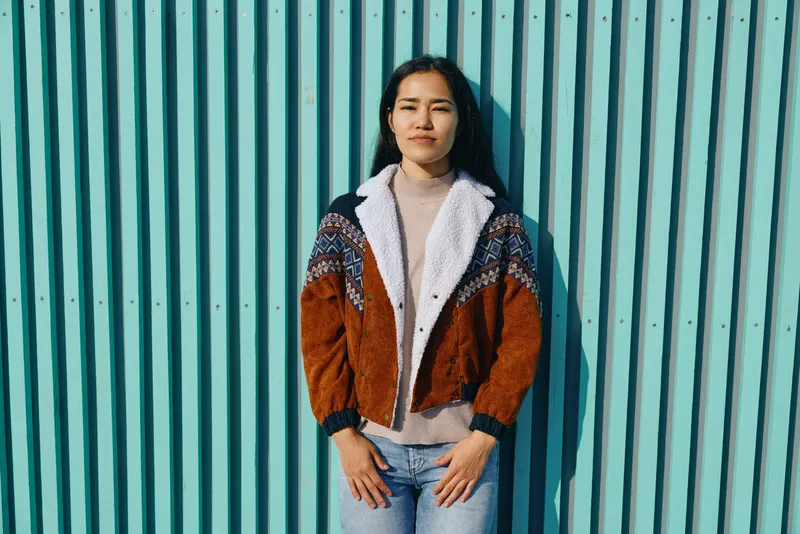 Woman wearing a cozy colorblock cardigan and beige turtleneck stands against a turquoise striped wall, showcasing casual streetstyle, fashion confidence, and urban chic.