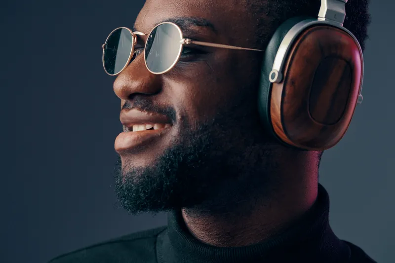 Stylish young man wearing headphones and sunglasses, showcasing a confident expression, with a modern dark background highlighting his trendy look and love for music