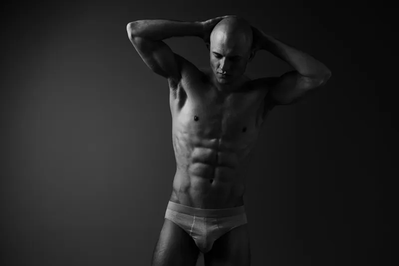 Black and white image of a muscular man posing confidently, showcasing his toned physique and strength, capturing the essence of fitness and determination.