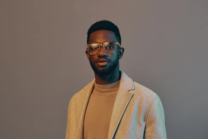 Confident African American man wearing glasses in a stylish neutral outfit against a muted background, embodying modern professionalism and elegance
