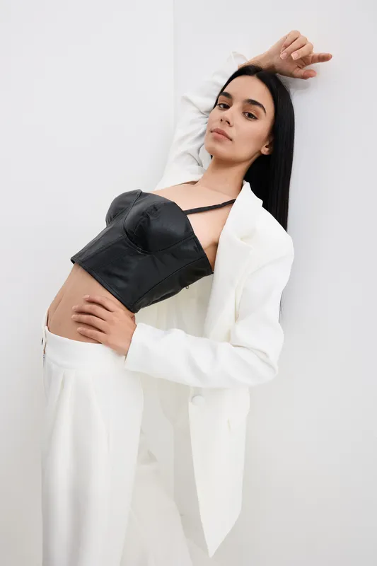 woman posing dressed in black leather top and white suit with stylish confident expression in minimalistic studio setting