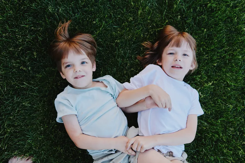 Playful children lying on grass, enjoying a sunny day. Their expressions reflect happiness and innocence, creating a cheerful atmosphere.