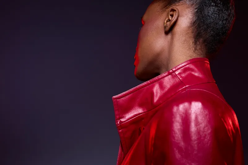 Portrait of a dark skinned African woman wearing a red leather jacket, shown from the back against a dark purple background. Concept of fashion, style, elegance, and confidence.