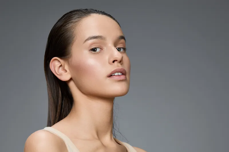 Elegant portrait of a young model with long hair, showcasing natural beauty and soft expression against a gray background, ideal for health and beauty themes