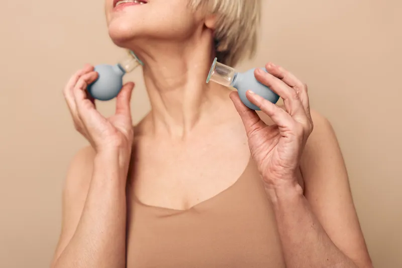 Mature woman with short hair using facial massage cups on neck and jawline, promoting skincare and anti-aging routine. Concept for self-care, beauty, and wellness at home.