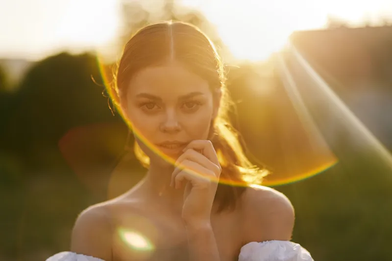 Young woman with a soft smile in golden sunset light, wearing an elegant off shoulder dress, radiating warmth and serenity, perfect for outdoor portraits