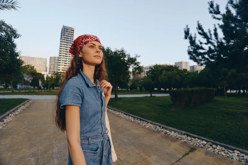 lifestyle woman wearing modern boho-western denim street style with a red bandana walking in an urban park with film color tones and natural light