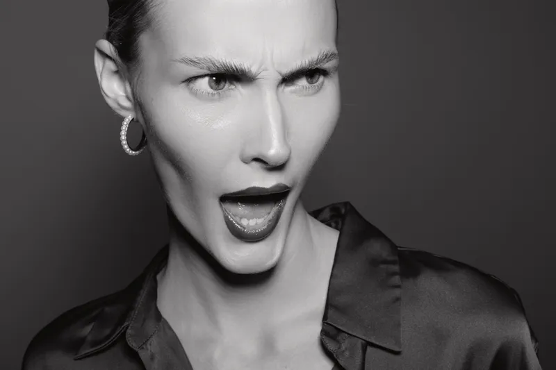 Angry caucasian woman with short hair and hoop earrings shouting in black blouse. Close-up portrait in monochrome. Concept of frustration, emotion, and female expression.