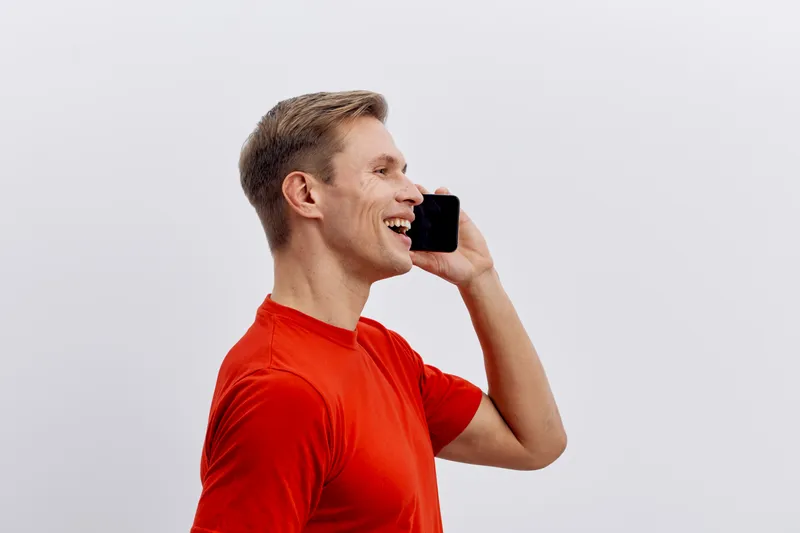 smiling man talking phone casual red tshirt side view white background digital nomad communication concept