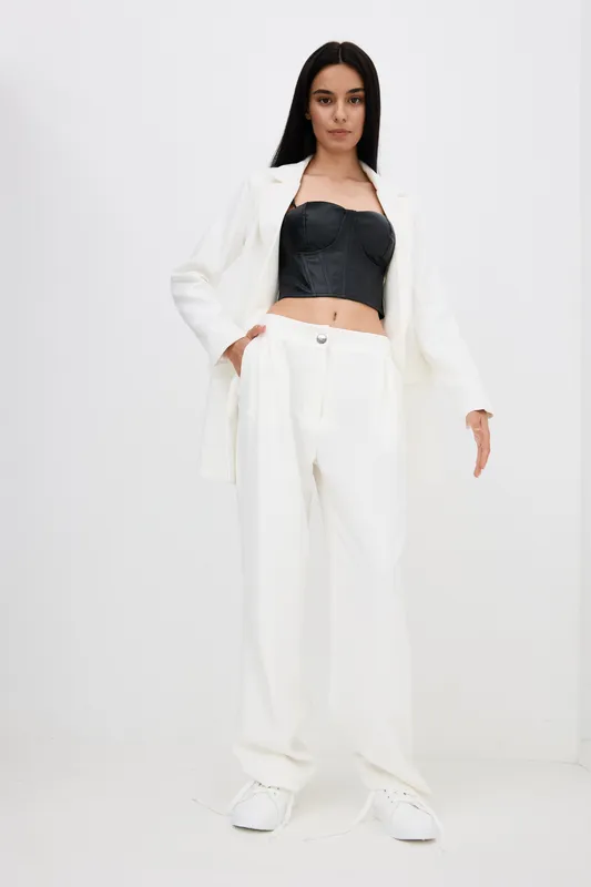 young woman wearing white suit and black corset standing confidently against clean background in stylish modern outfit combining casual and formal elements