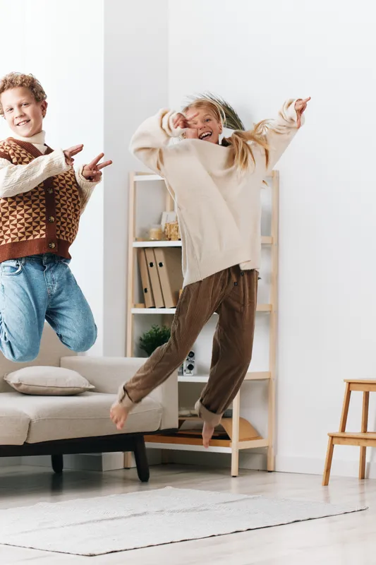 Authentic moment of playful youths in a home setting, capturing a school themed lifestyle scene as they jump with joy, showcasing carefree energy and real life interaction.