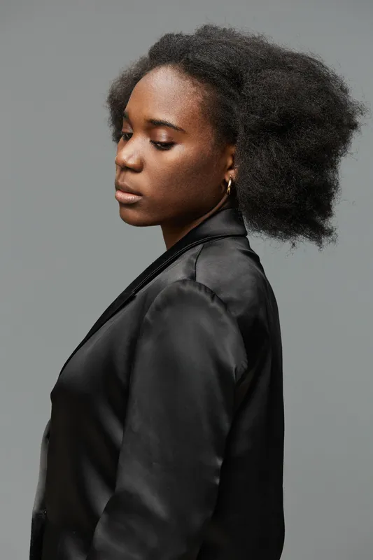 Woman with natural afro hairstyle in a sleek black blazer, showcasing confidence and elegance against a neutral gray background